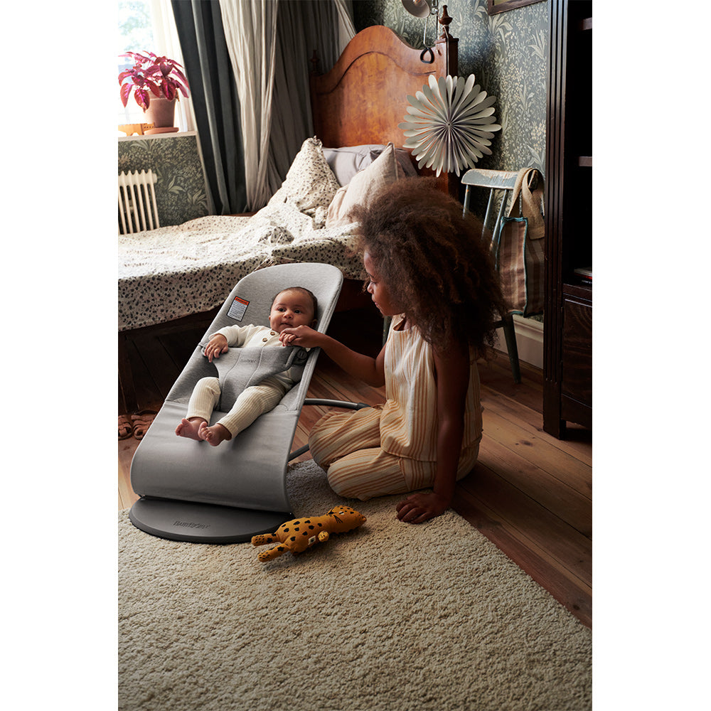 Sister sitting no the floor nnext to baby in BABYBJÖRN Bouncer Bliss in -- Color_Light Gray 3D Jersey