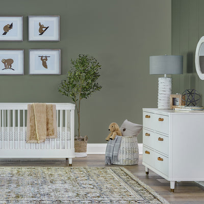 Namesake's Tanner 3-in-1 Convertible Crib with a blanket over the rail and next to a dresser 