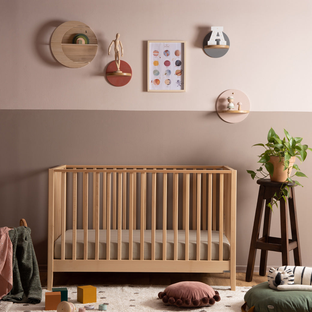 Dadada Lala 3-in-1 Convertible Crib next to a stool with a potted plant  in - Color_Natural