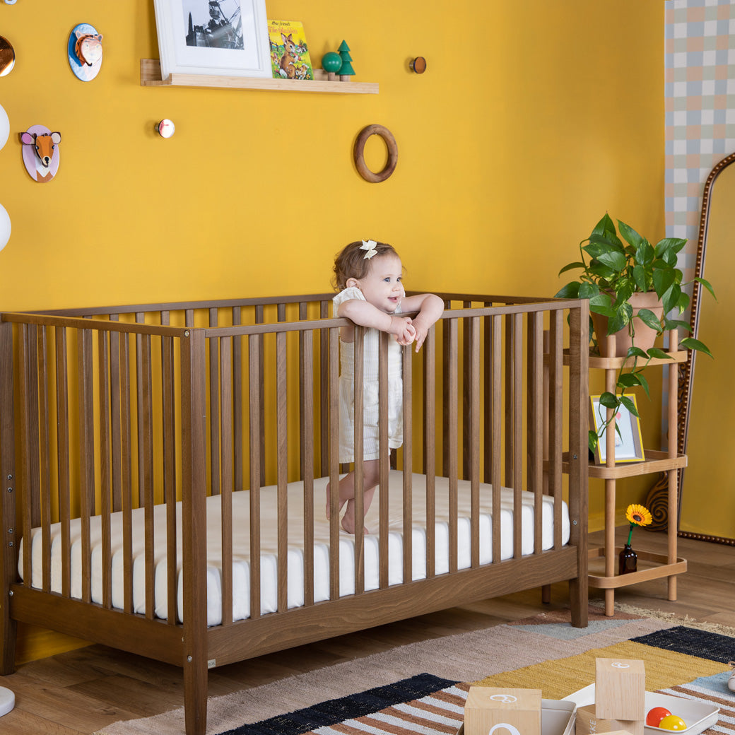 Child smiling in the Dadada Lala 3-in-1 Convertible Crib in - Color_Walnut