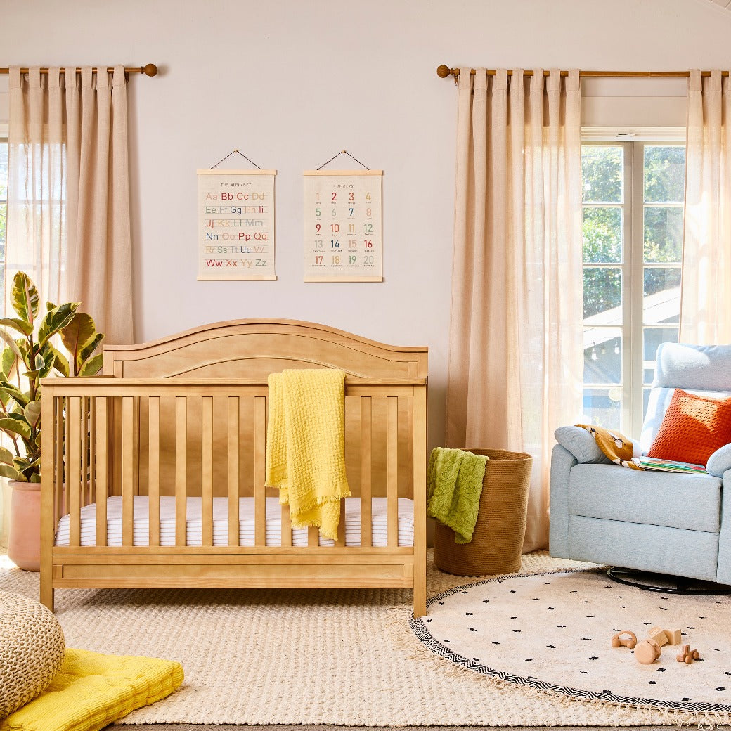 The DaVinci Charlie 4-in-1 Convertible Crib next to recliner in -- Color_Honey