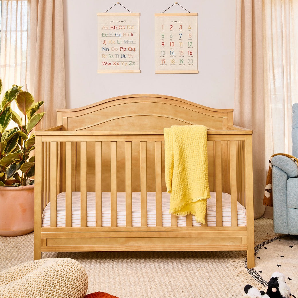 The DaVinci Charlie 4-in-1 Convertible Crib with yellow blanket over the rail in -- Color_Honey