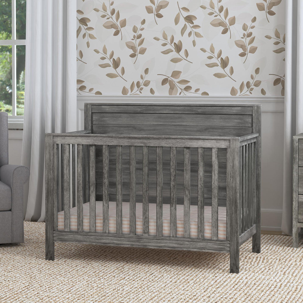 DaVinci Fairway 4-in-1 Convertible Crib next to a recliner in -- Color_Cottage Grey