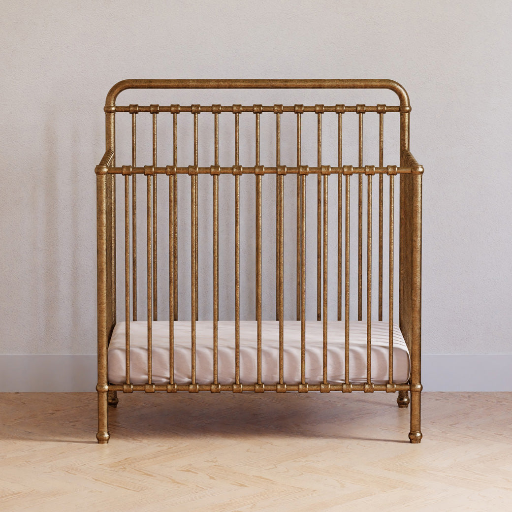 Front view of Namesake's Winston 4-in-1 Convertible Mini Crib in a room in -- Color_Vintage Gold