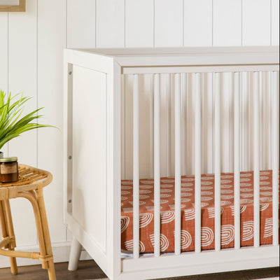 Closeup of Babyletto's Peggy 3-in-1 Convertible Crib next to a table in -- Color_Warm White