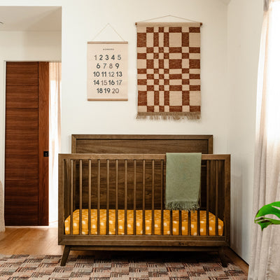 Front view of Babyletto's Palma 4-in-1 Convertible Crib under two wall hangings in -- Color_Natural Walnut