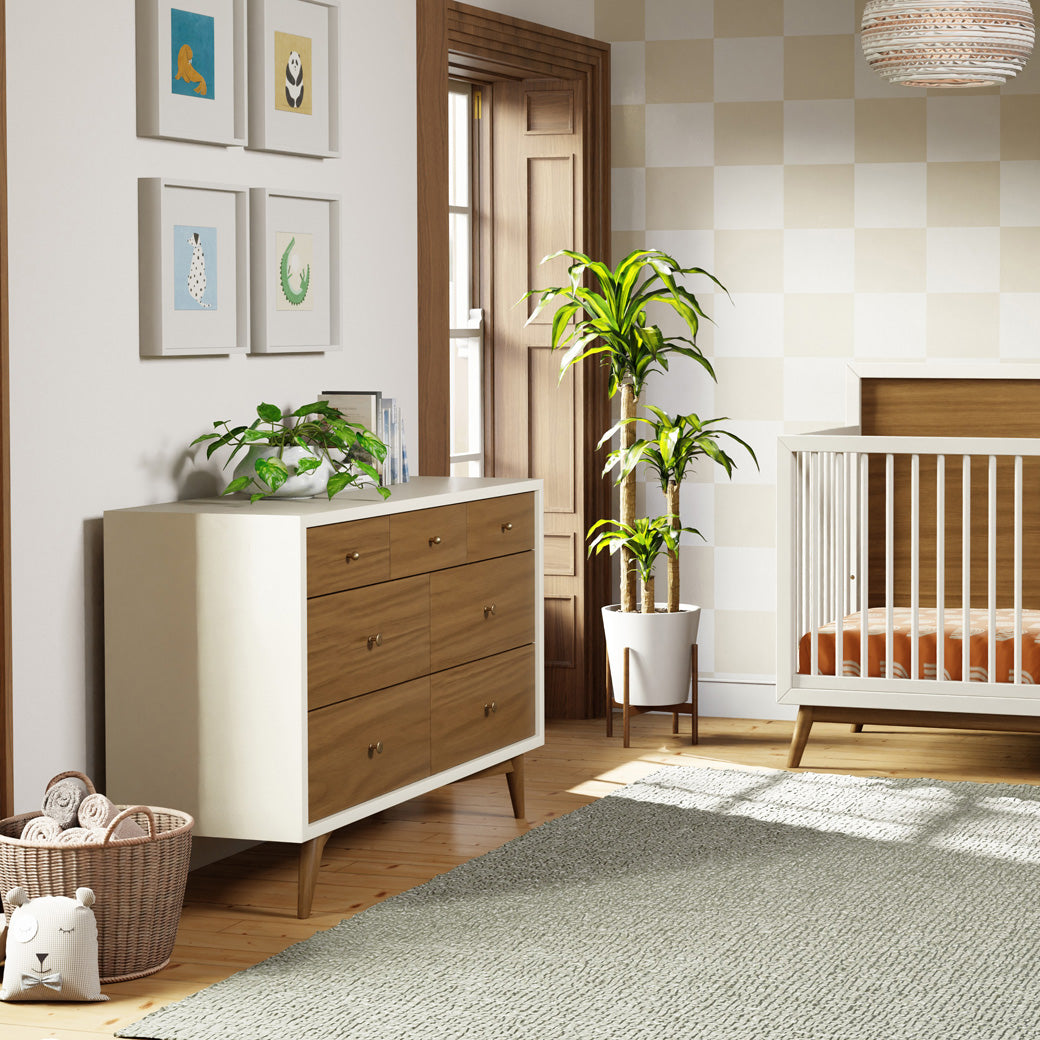 Babyletto's Palma 7-Drawer Assembled Double Dresser next to a window and Palma crib  in -- Color_Warm White with Natural Walnut