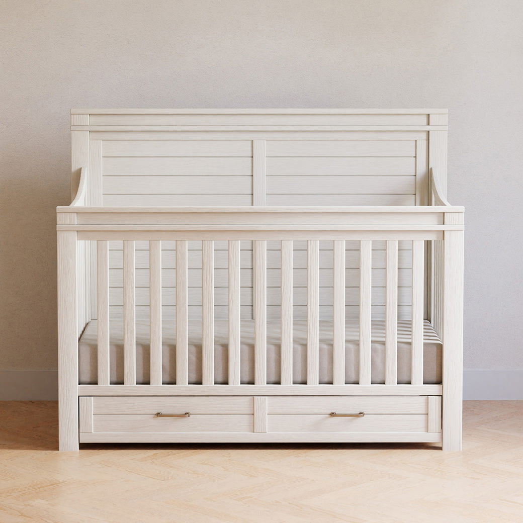 Front view of Namesake's Wesley Farmhouse 4-in-1 Convertible Storage Crib in a room in -- Color_Heirloom White