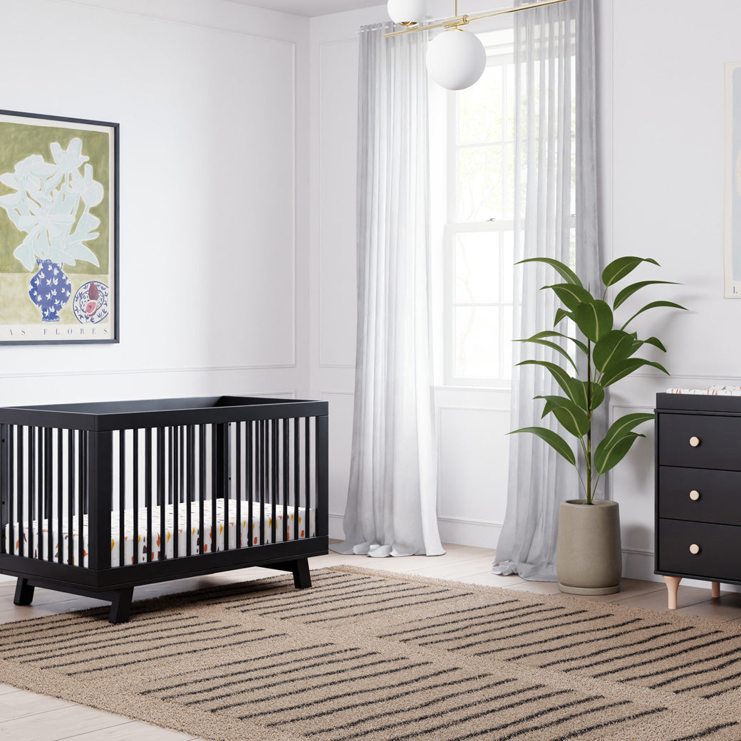 Babyletto Hudson 3-in-1 Crib next to a window, plant, and dresser  in -- Color_Black