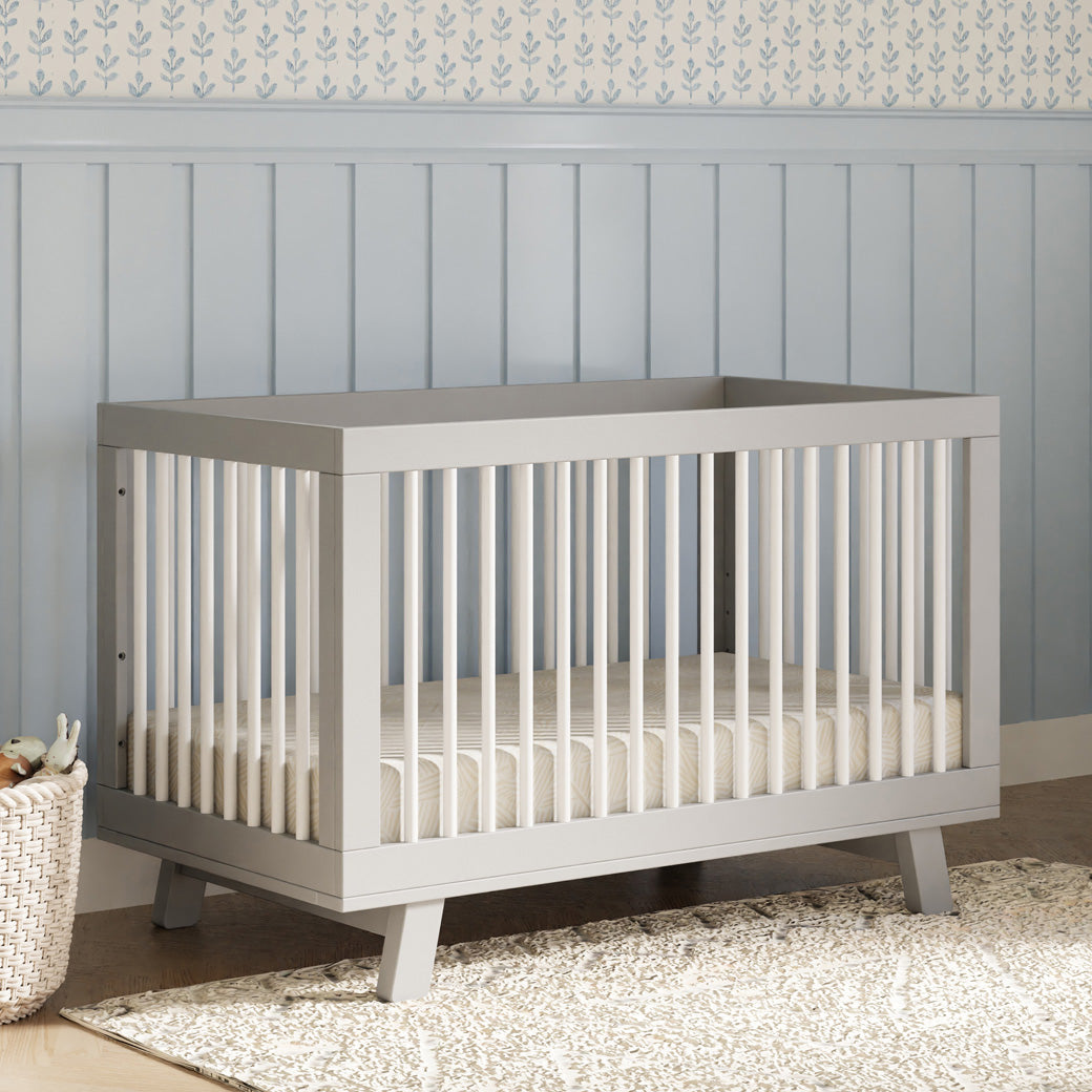 Babyletto Hudson 3-in-1 Convertible Crib + Toddler Rail next to a basket in -- Color_White/Grey