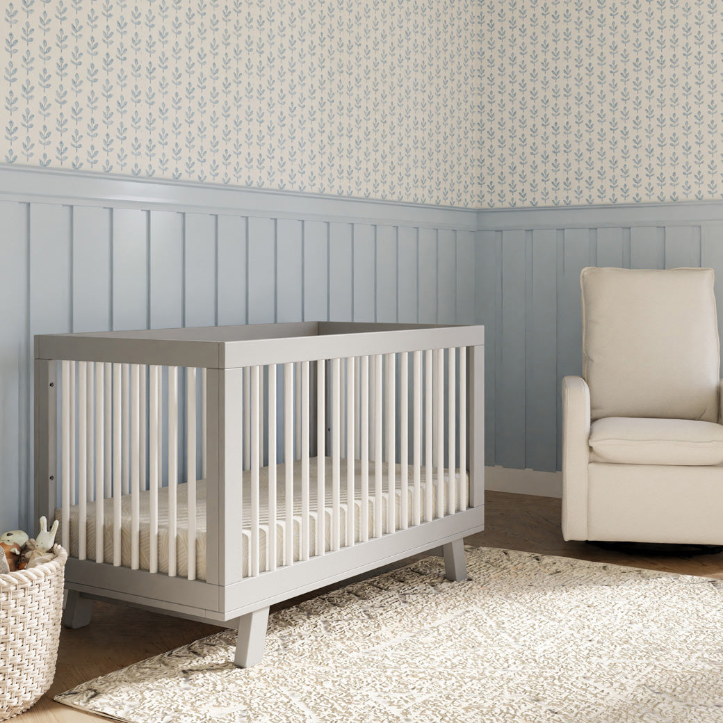 Babyletto Hudson 3-in-1 Convertible Crib + Toddler Rail next to a recliner  in -- Color_White/Grey