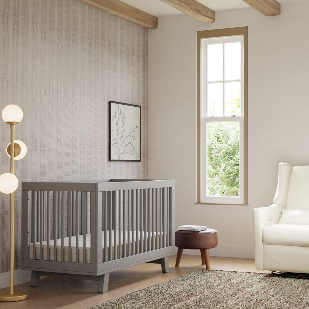 Babyletto Hudson 3-in-1 Crib next to a lamp, stool, and recliner  in -- Color_Grey