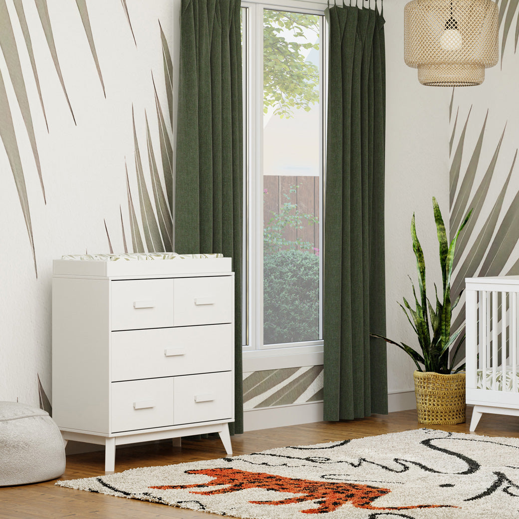 Babyletto's Scoot 3-Drawer Changer Dresser next to a window and crib in -- Color_White