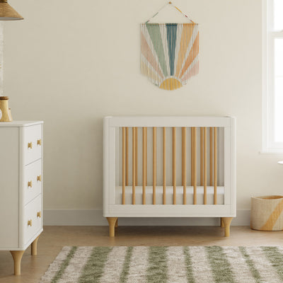 Front view of The Babyletto Lolly 4-in-1 Convertible Mini Crib next to a dresser in -- Color_White / Natural