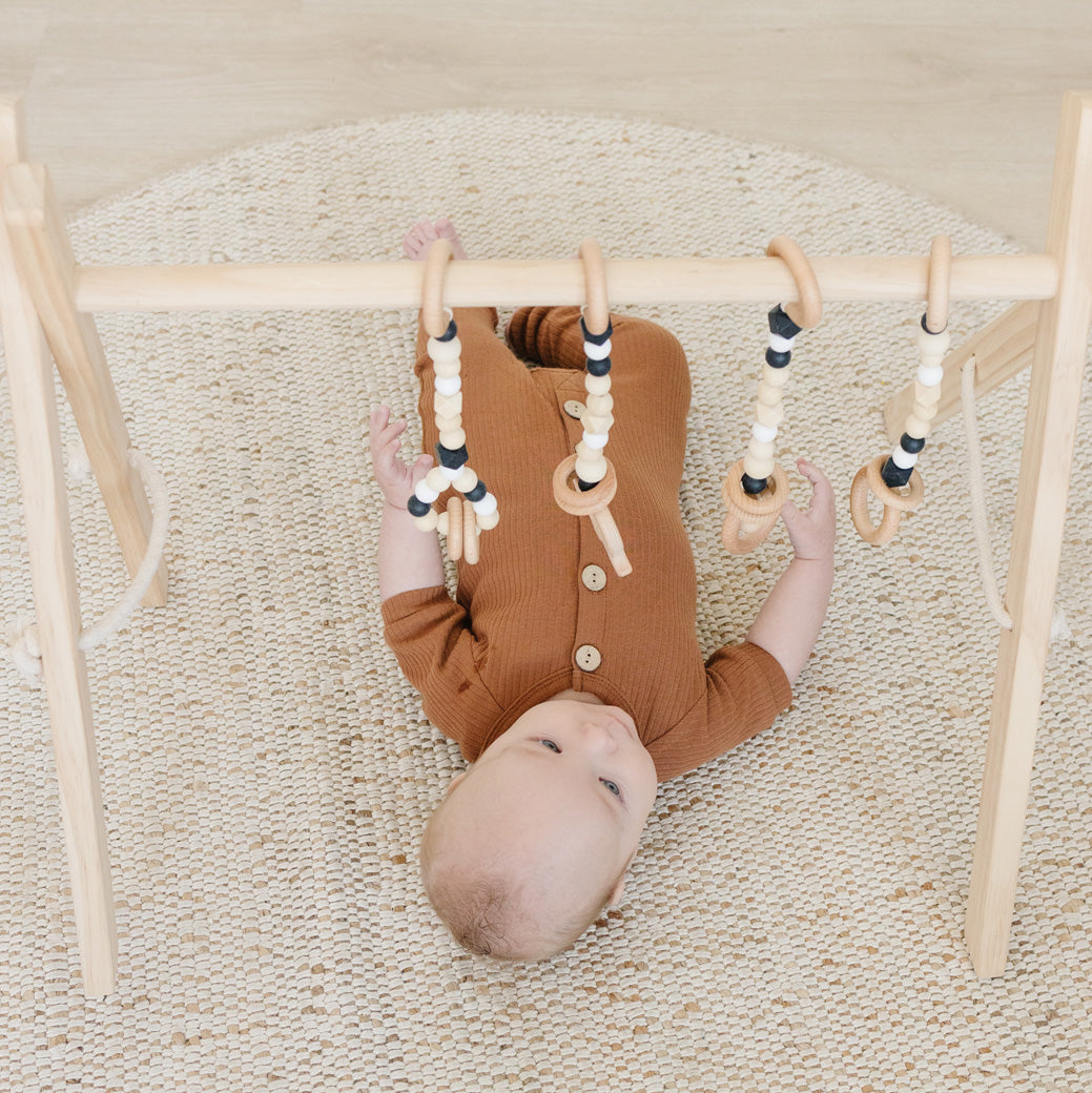 Top view of baby playing with Poppyseed Play Wood Baby Gym + Toys in -- Color_Natural _ Black