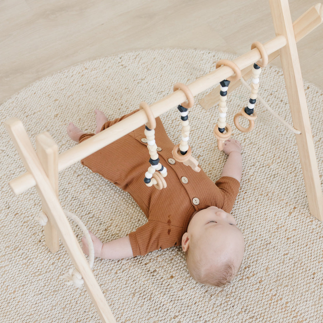 Baby laying and playing with Poppyseed Play Wood Baby Gym + Toys in -- Color_Natural _ Black