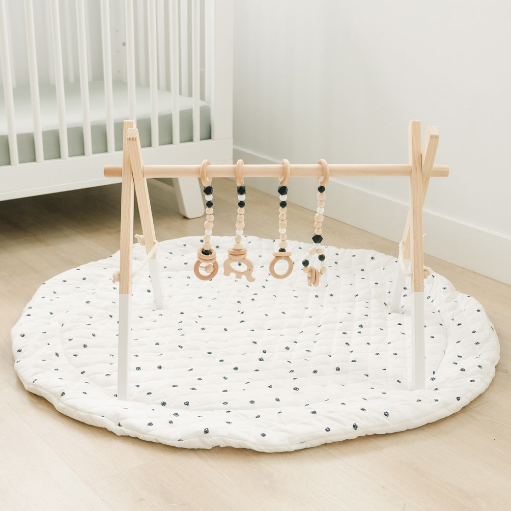 Poppyseed Play Wood Baby Gym + Toys on a white spotted mat in -- Color_Natural _ Black