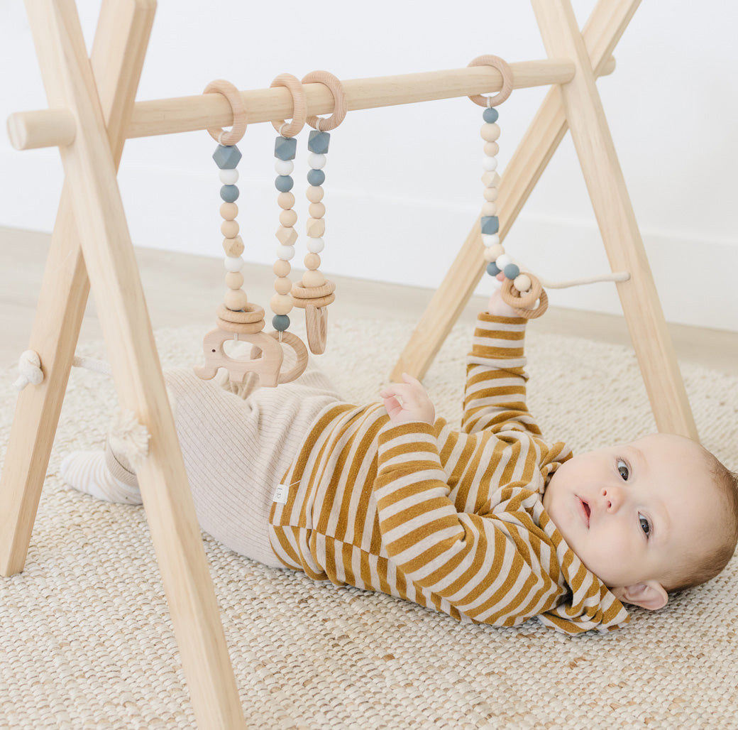 Baby playing on Poppyseed Play Wood Baby Gym + Toys in -- Color_Natural _ Gray
