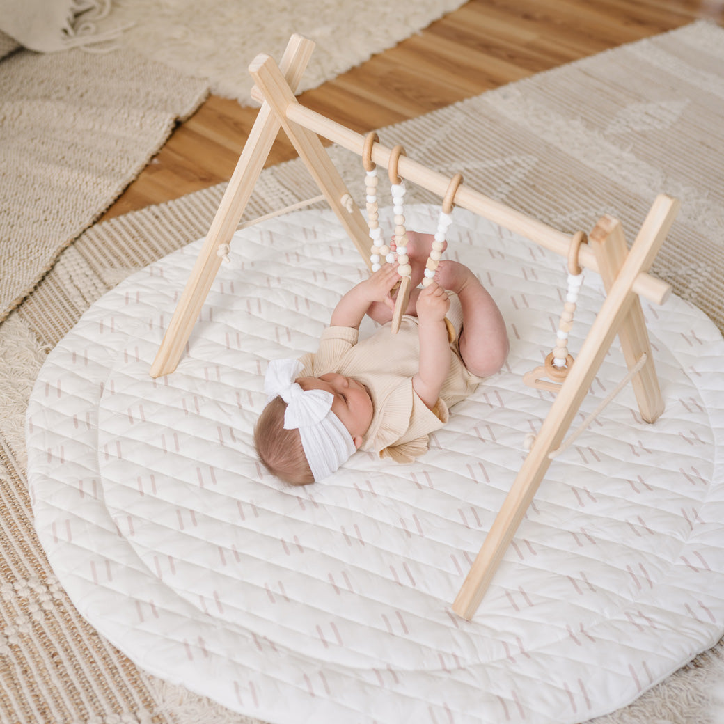 Baby laying on mat playing with Poppyseed Play Wood Baby Gym + Toys in -- Color_Natural _ White