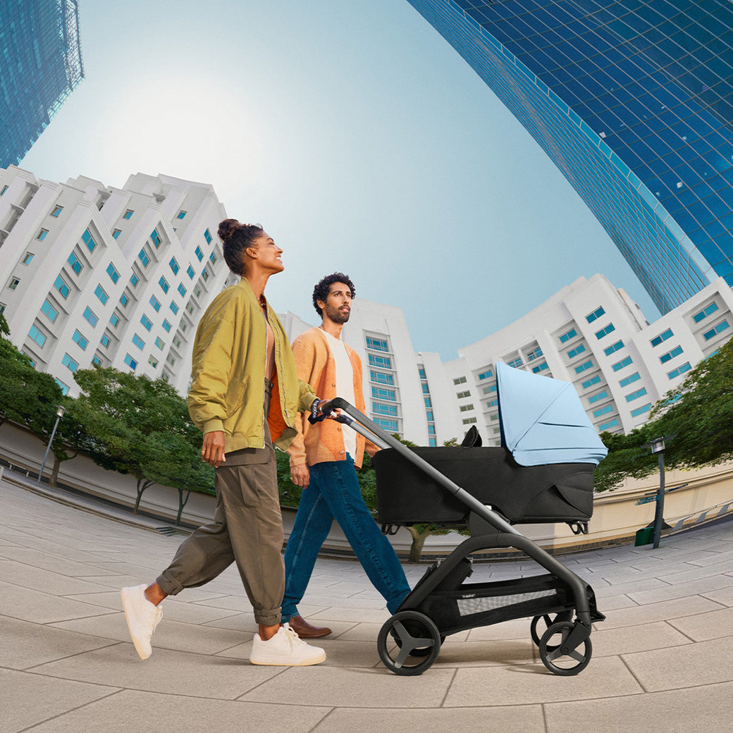 Mom and dad pushing their baby in the Bugaboo Dragonfly Stroller With Bassinet in -- Color_Skyline Blue