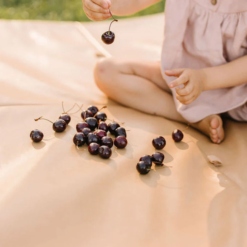 A child with cherries on the Toki Mats Vegan Leather Play Mat in -- Color_Sand