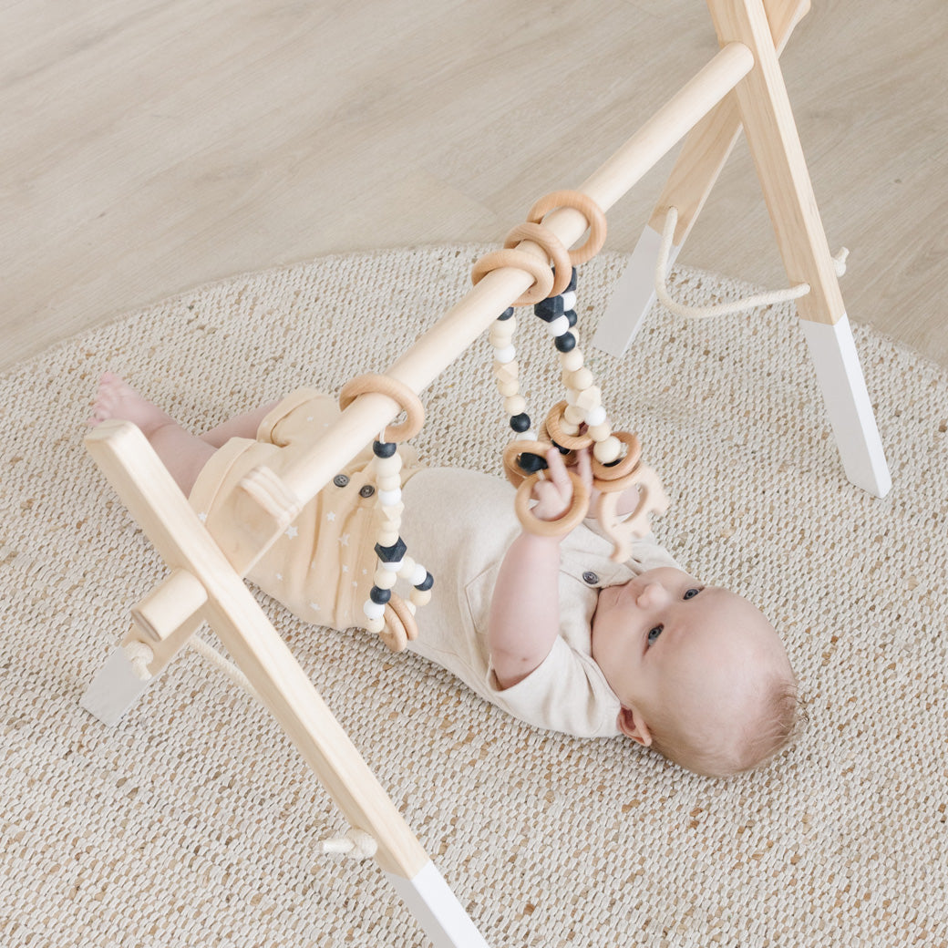 Baby holding toys and playing with Poppyseed Play Wood Baby Gym + Toys in -- Color_White _ Black