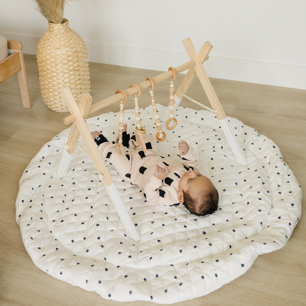 Baby laying and playing with Poppyseed Play Wood Baby Gym + Toys in -- Color_White _ Wood
