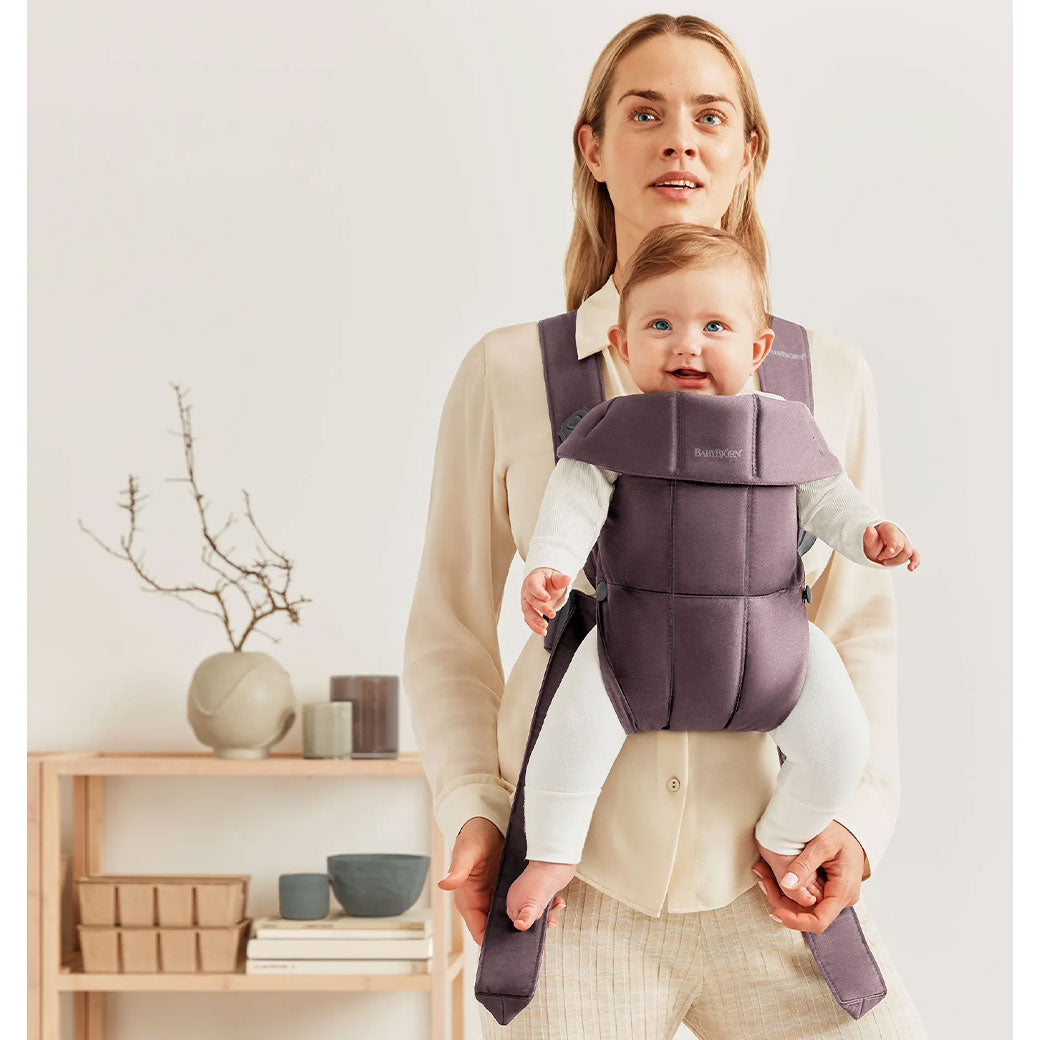 Front view of mom carrying baby in BABYBJÖRN Baby Carrier Mini with top part down in -- Color_Dark Purple Woven