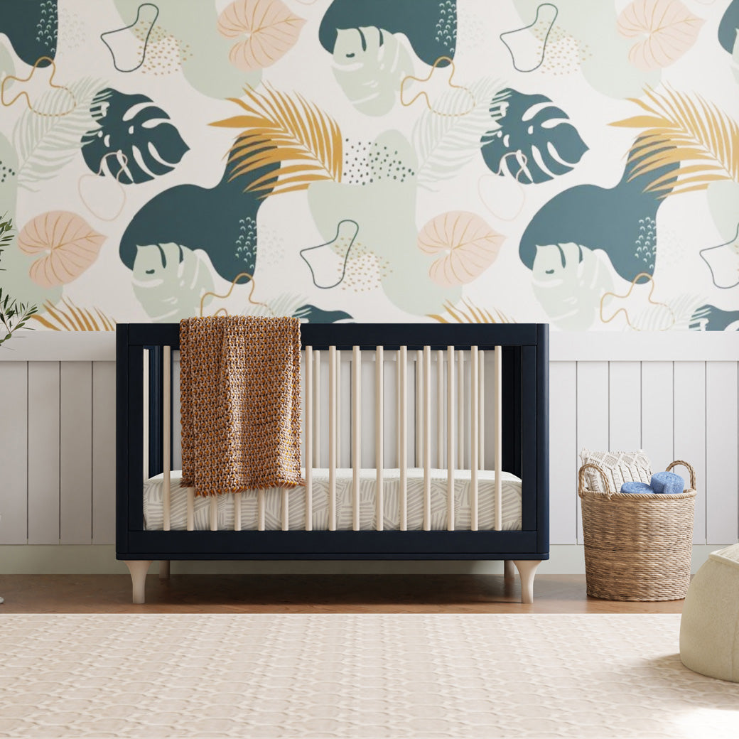 The Babyletto Lolly 3-in-1 Crib with blanket on rail next to a basket  in -- Color_Navy