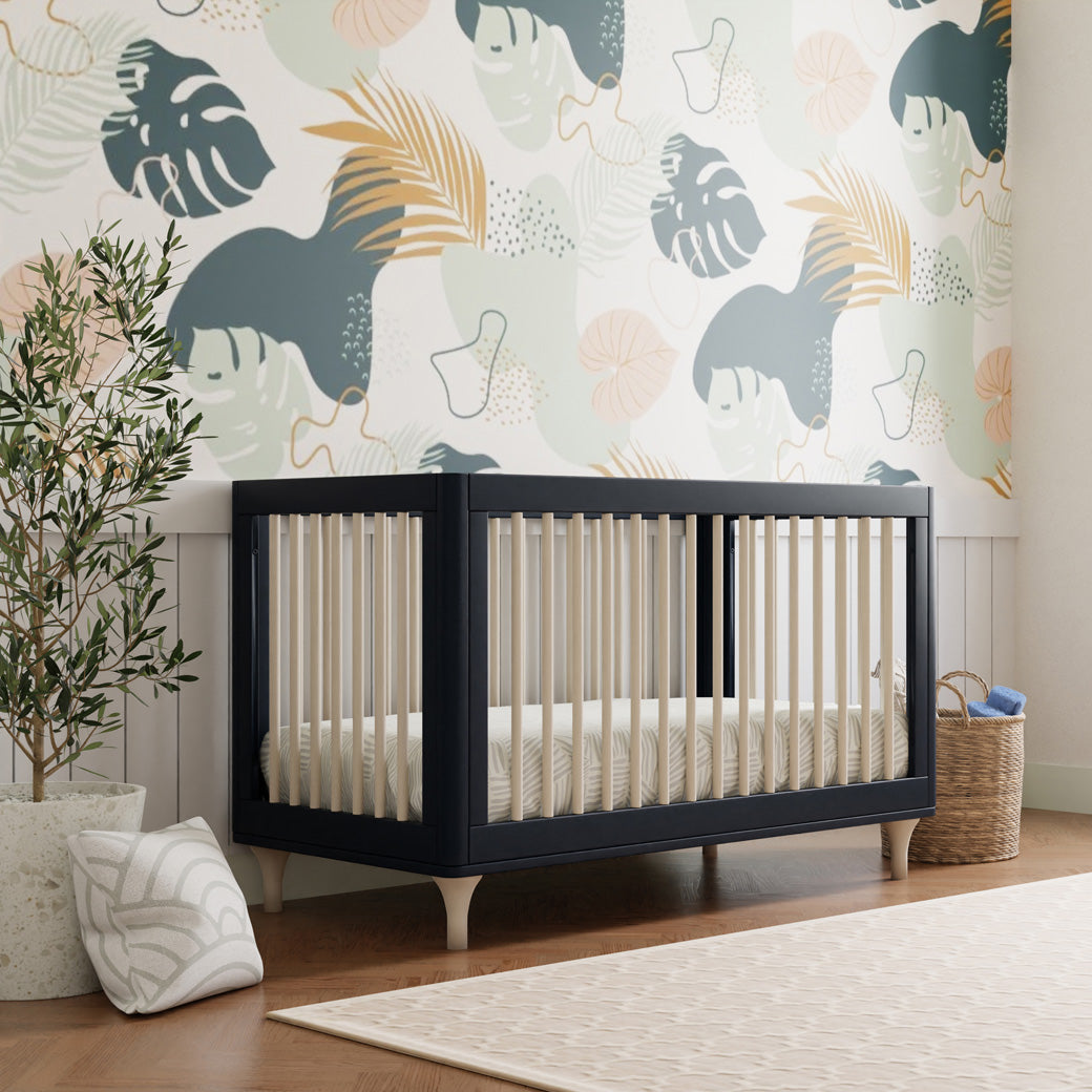 The Babyletto Lolly 3-in-1 Crib next to a plant and basket in -- Color_Navy