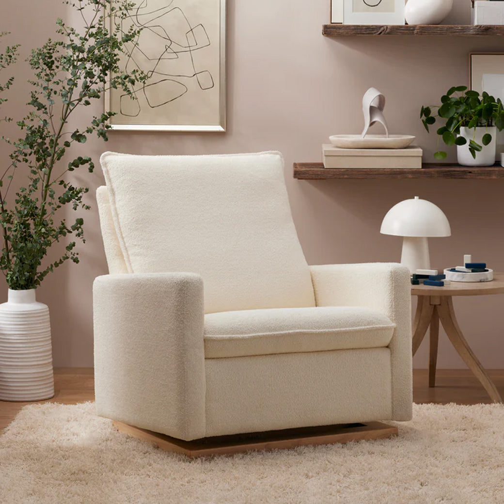 Babyletto Cali Pillowback Chair-and-a-Half Glider next to plant and coffee table  in -- Color_Chantilly Sherpa with Light Wood Base