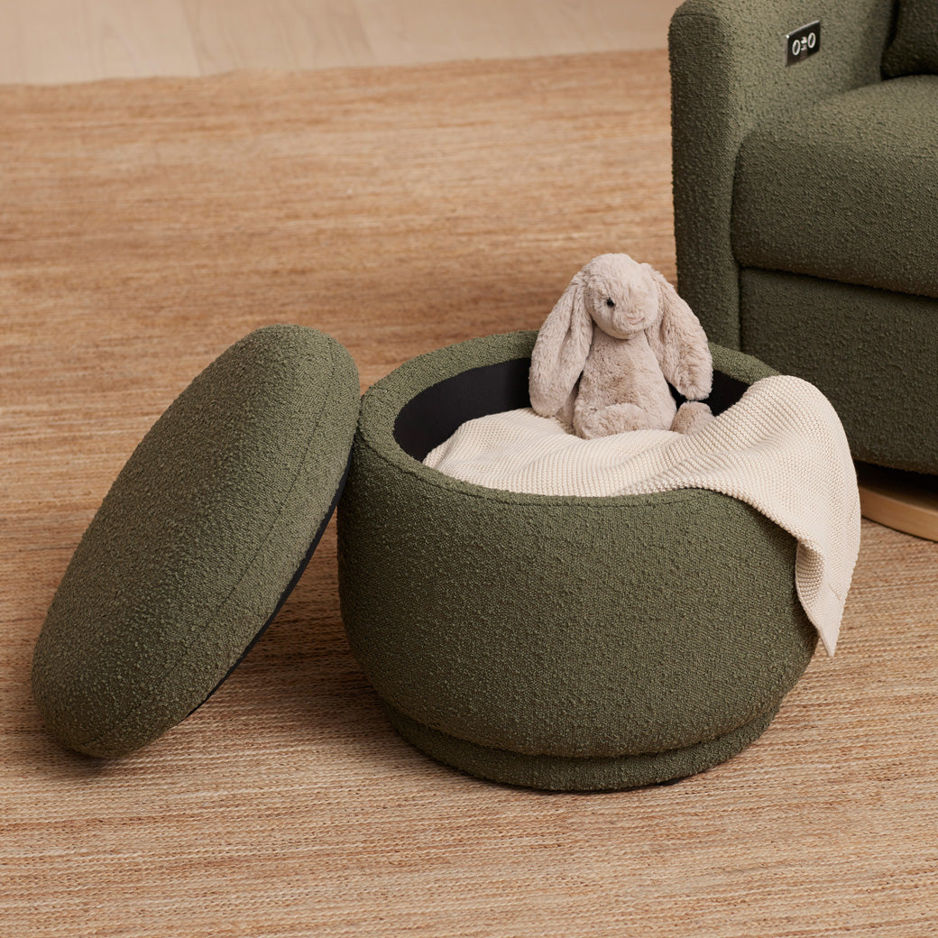 The Babyletto Enoki Storage Ottoman with a blanket and a toy rabbit inside  in --Color_Olive Boucle