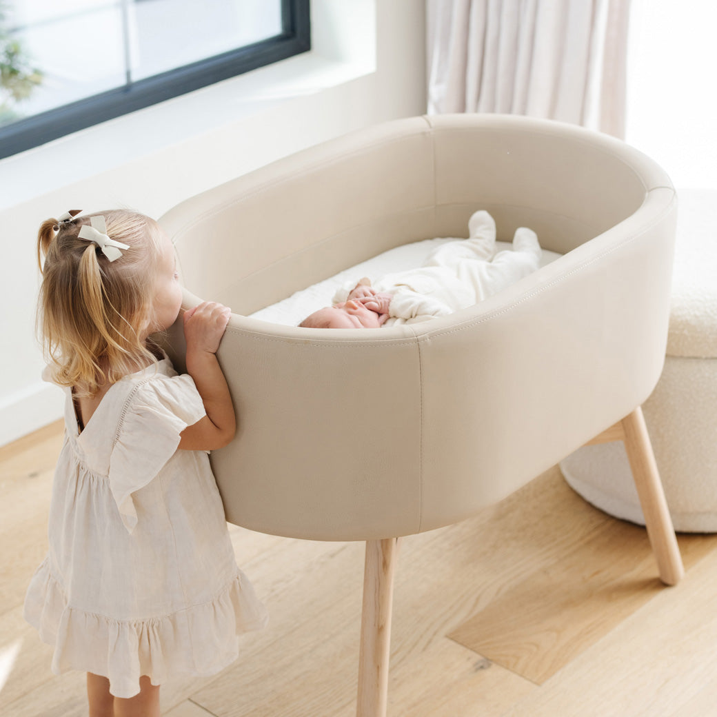 Toddler looking at baby in the Babyletto GATHRE Capsule Bassinet in -- Color_Millet