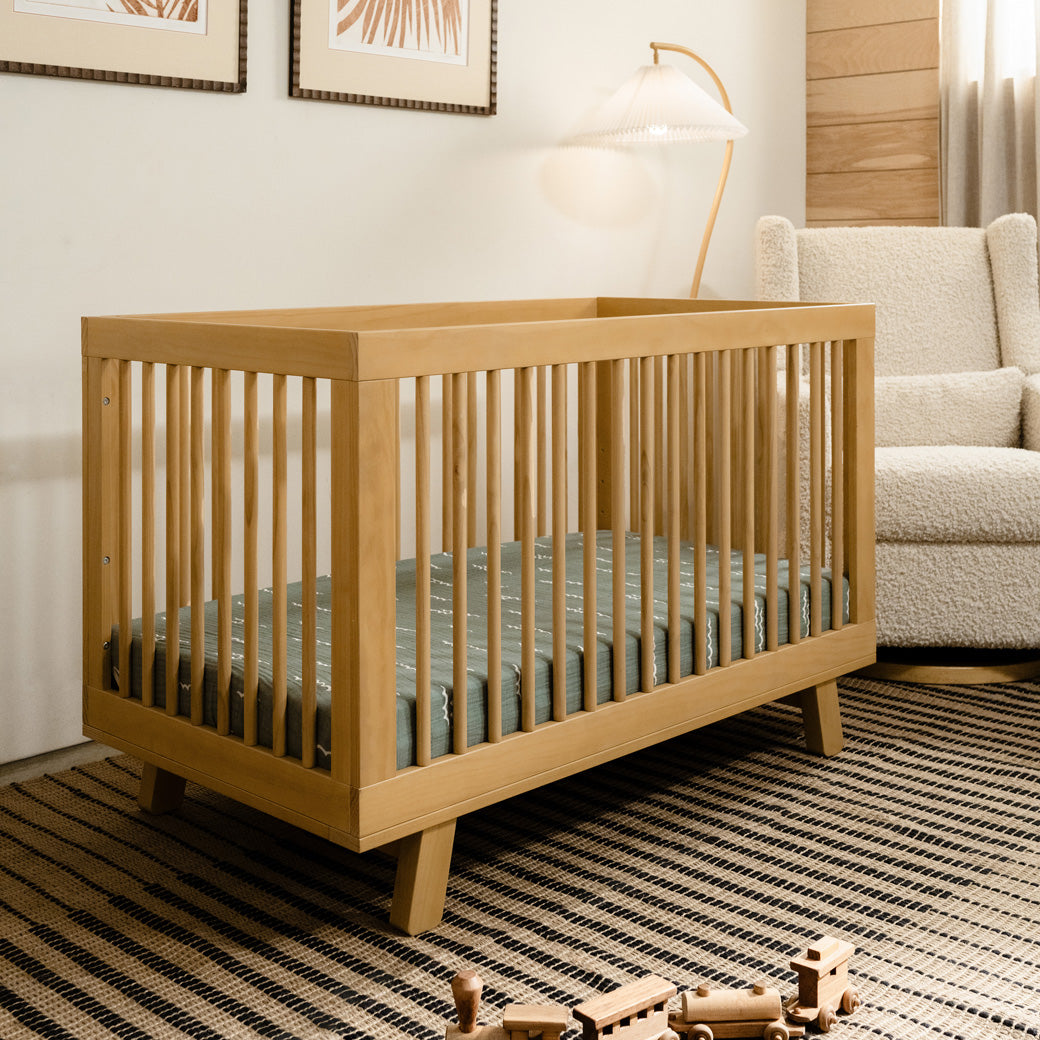 Babyletto Hudson 3-in-1 Convertible Crib And Toddler Rail next to a recliner in -- Color_Honey