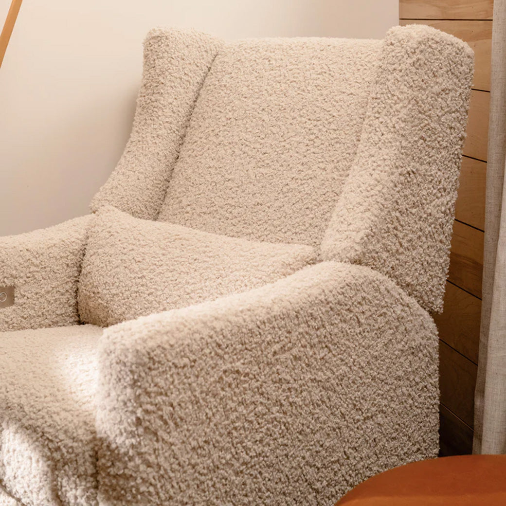 Closeup of Babyletto Kiwi Glider Recliner next to ottoman  in -- Color_Almond Teddy Loop with Light Wood Base