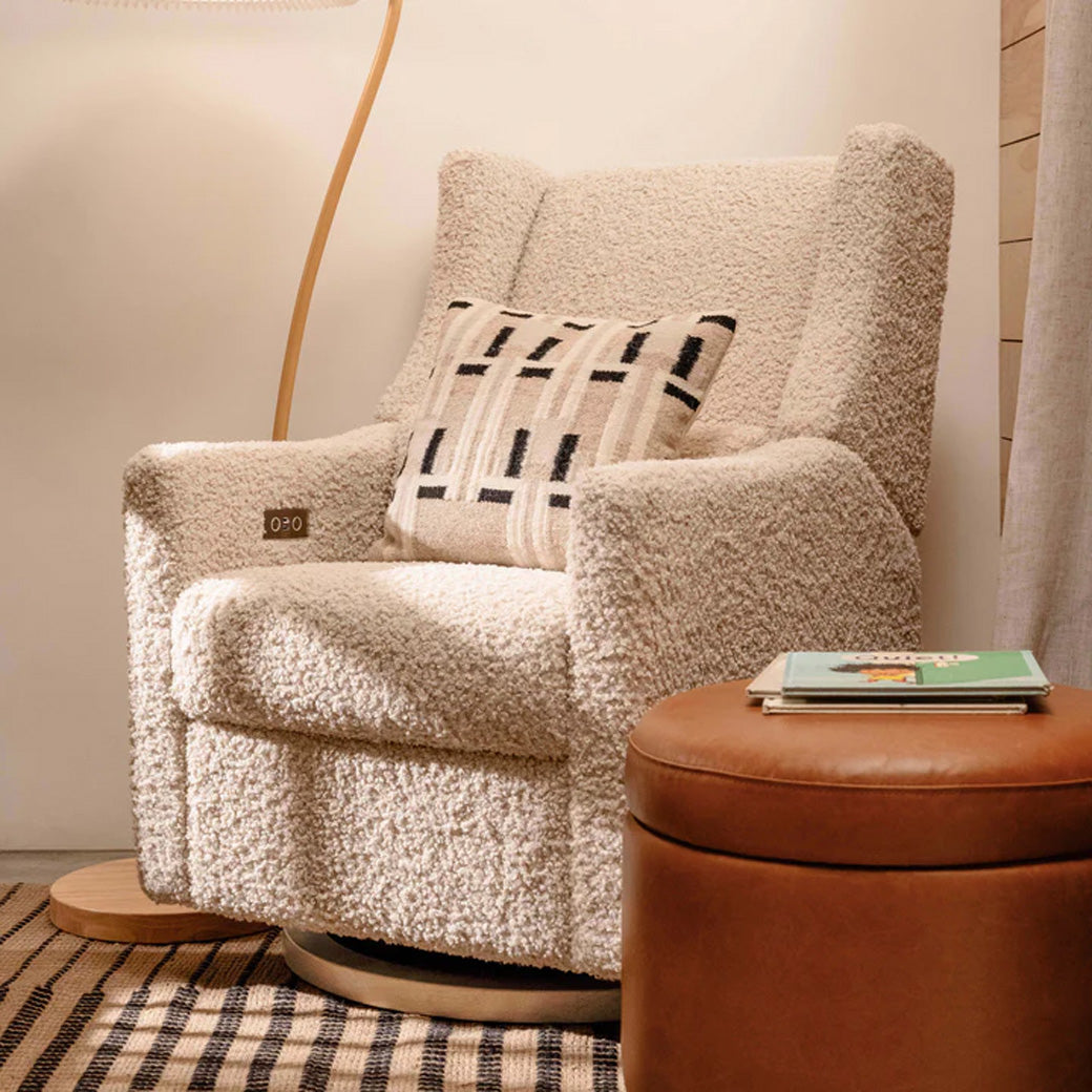 Babyletto Kiwi Glider Recliner with a pillow and next to ottoman in -- Color_Almond Teddy Loop with Light Wood Base