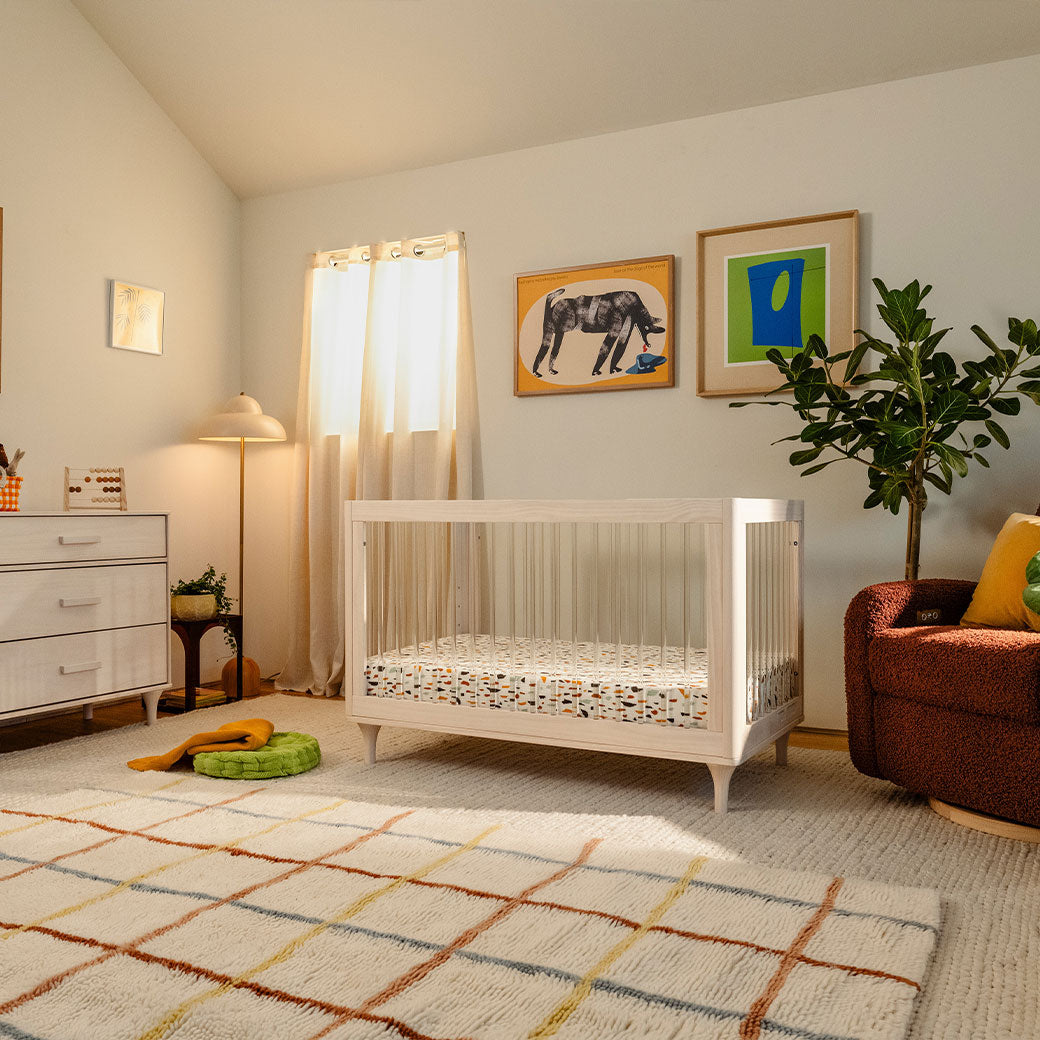 The Babyletto Lolly 3-in-1 Convertible Crib next to a recliner and dresser in -- Color_Washed Natural / Acrylic