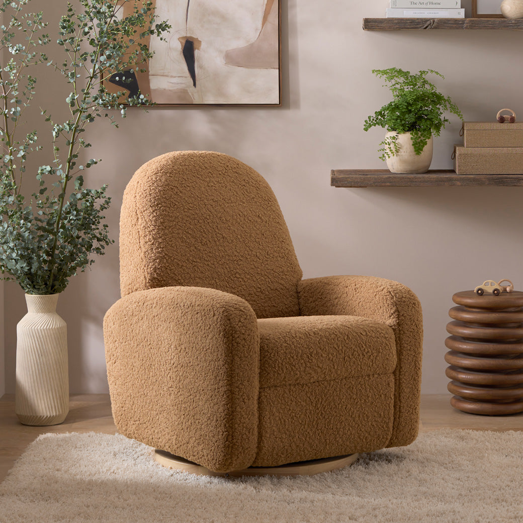 The Babyletto Nami Glider Recliner next to a plant and shelf in -- Color_Cortado Shearling with Light Wood Base