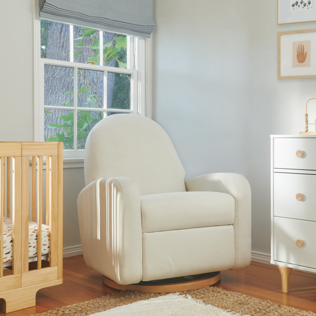 Babyletto Nami Glider Recliner next to a crib and dresser  in -- Color_Performance Cream Eco-Weave with Light Wood Base