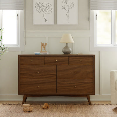 Front view of Babyletto's Palma 7-Drawer Assembled Double Dresser with a lamp on top in -- Color_Natural Walnut