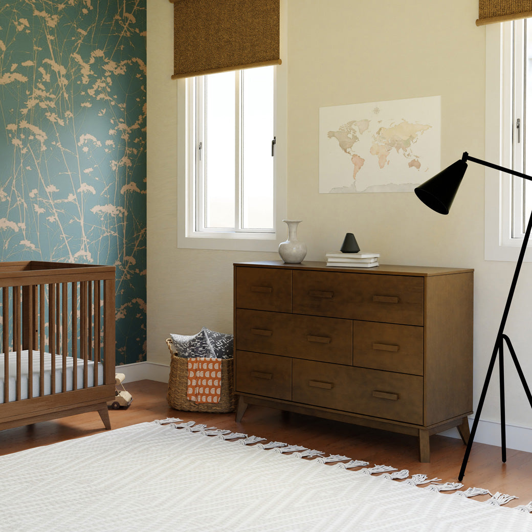 Babyletto Scoot 6-Drawer Dresser next to a basket and crib in -- Color_Natural Walnut