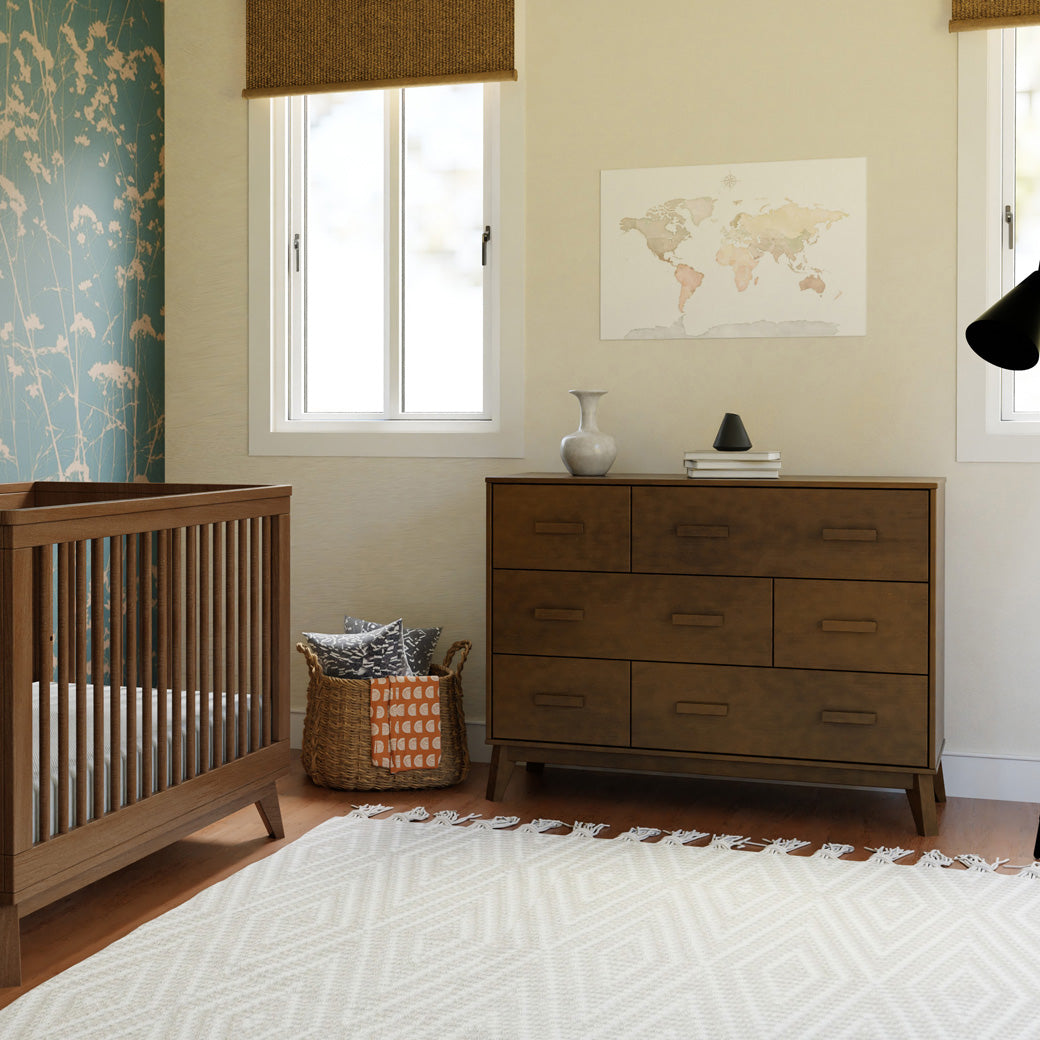 Front view of Babyletto Scoot 6-Drawer Dresser next to basket and crib in -- Color_Natural Walnut