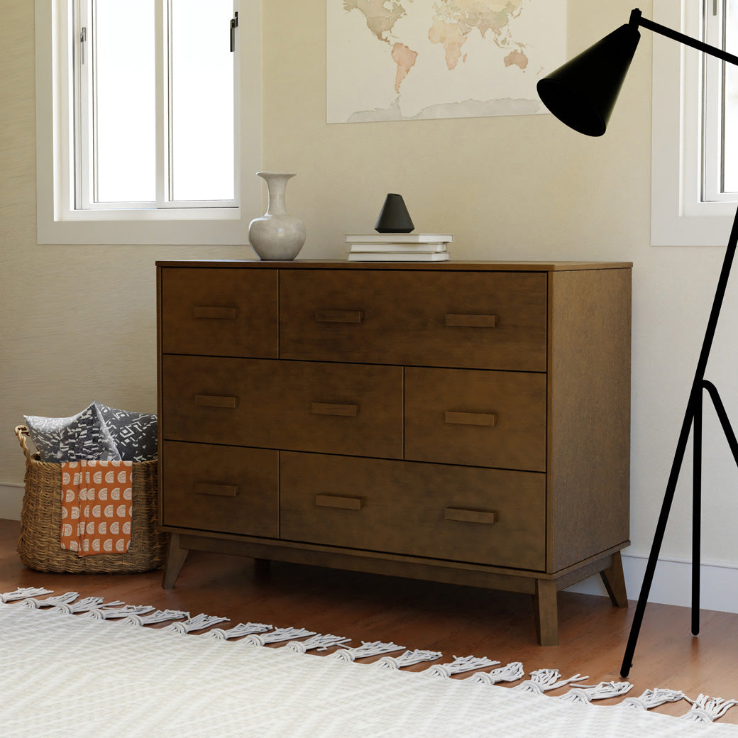Babyletto Scoot 6-Drawer Dresser next to a basket and lamp in -- Color_Natural Walnut