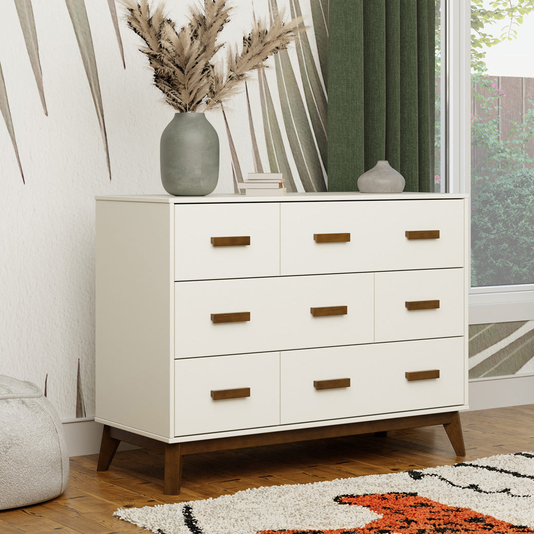 Babyletto Scoot 6-Drawer Dresser next to a window with decorations on top in -- Color_White / Natural Walnut