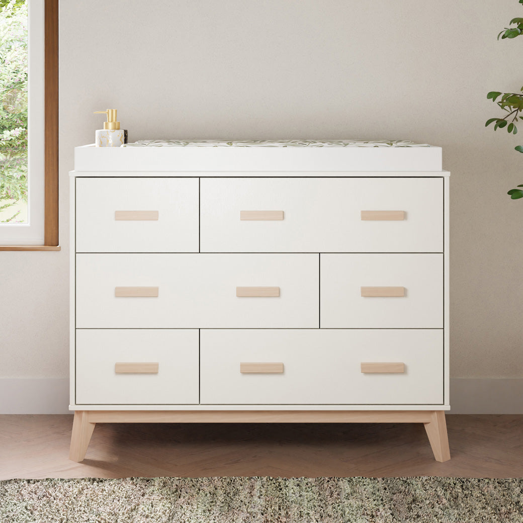 Front view of Babyletto Scoot 6-Drawer Dresser with changing tray next to a window and plant  in -- Color_White / Washed Natural