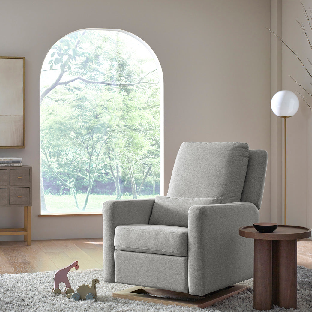 Babyletto Sigi Glider Recliner in front of a window and next to a coffee table in -- Color_Performance Grey Eco-Weave with Light Wood Base