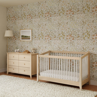 Babyletto's Sprout 4-in-1 Convertible Crib next to a dresser in a floral room in -- Color_Washed Natural / White