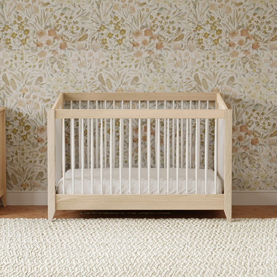 Front view of Babyletto's Sprout 4-in-1 Convertible Crib in a floral room in -- Color_Washed Natural / White