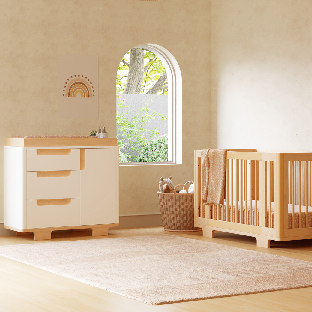Babyletto Yuzu 3-Drawer Changer Dresser next to a window and crib  in -- Color_White / Natural