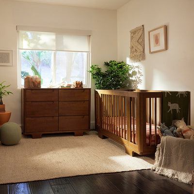 Babyletto Yuzu 6-Drawer Dresser under a window and next to a crib  in -- Color_Natural Walnut